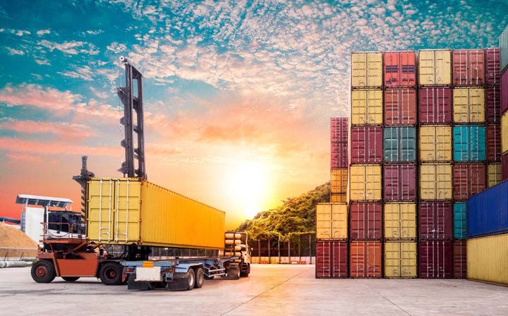 Shipping containers being loaded at a logistics yard at sunset