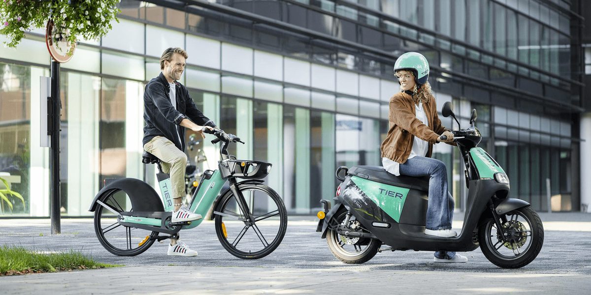 Riders on TIER e-bikes and scooters outside a glass office building